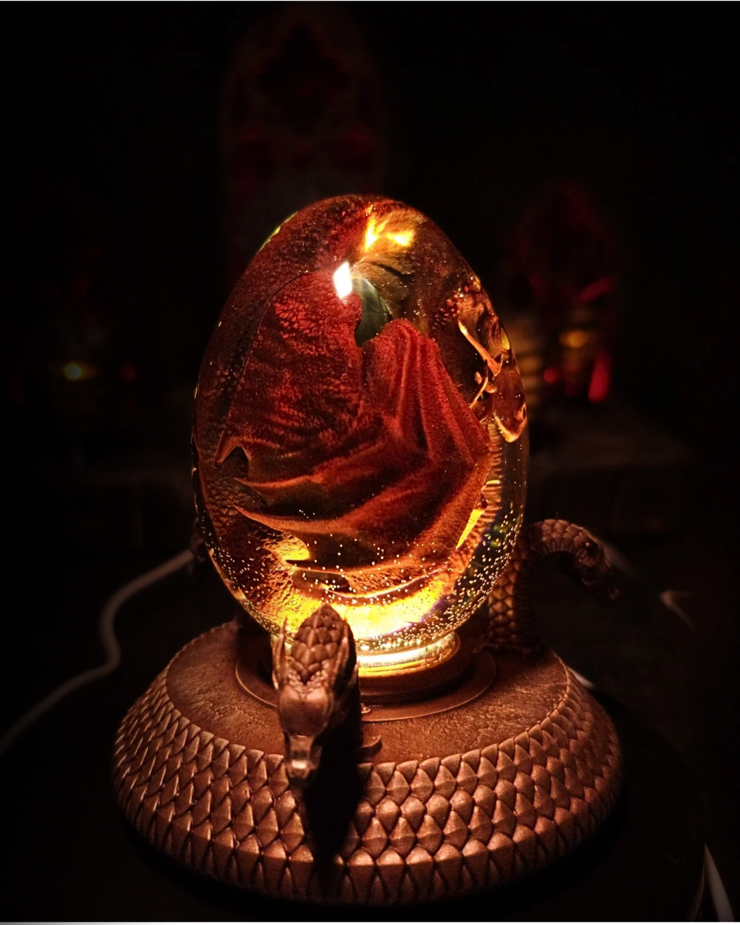 Œuf de résine abritant un dragon rouge enroulé - sculpture fantasy lumineuse avec socle bronze à tête de dragon