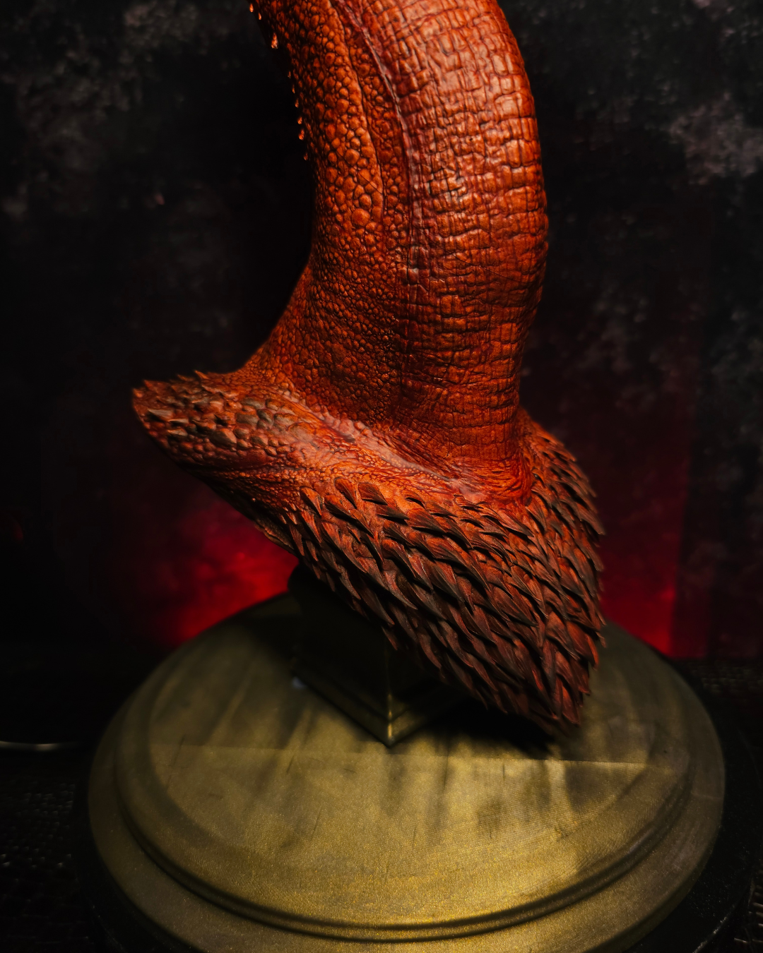 Détail de la partie inférieure du buste de dragon rouge montrant les textures d’écailles sculptées et le socle peint effet bronze vieilli.