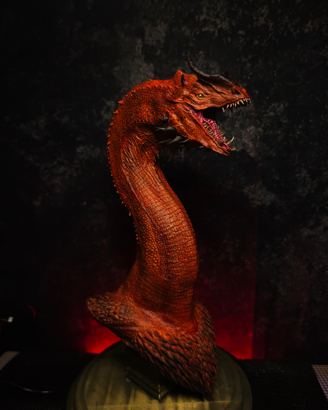 Buste de dragon rouge à la gueule ouverte photographié de trois quarts, mettant en valeur le cou, les écailles et les détails sculptés du modèle.