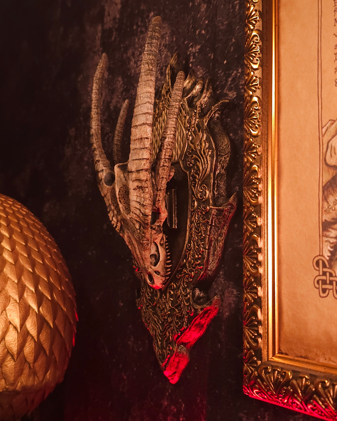 Crâne de dragon avec longues cornes verticales monté sur un support mural décoratif, éclairage rouge intense et décor intérieur fantasy sombre.