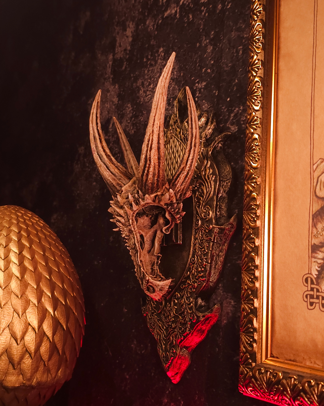 Crâne de dragon avec multiples cornes élancées monté sur un support mural ornemental, éclairage rouge et ambiance fantasy immersive.