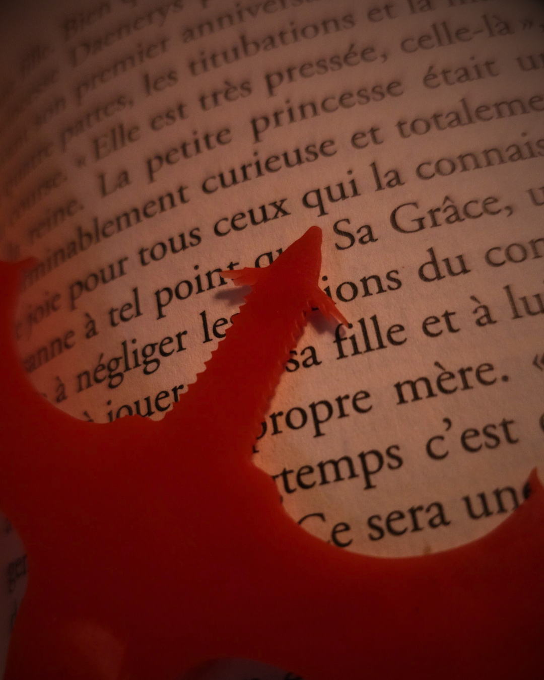 Gros plan du corps du marque-page Meleys en résine rouge, reposant sur les pages d’un roman de George R.R. Martin.