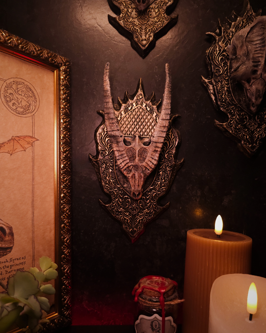 Mur décoratif présentant plusieurs trophées de crânes de dragons fantasy, dont un crâne doré, dans une composition gothique et médiévale.