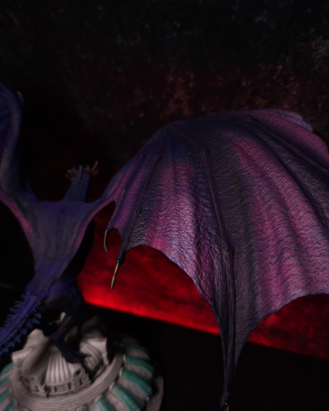 Gros plan sur les ailes de la figurine Dreamfyre en résine, montrant les membranes violettes et pourpres, les nervures sculptées et les griffes dorées.