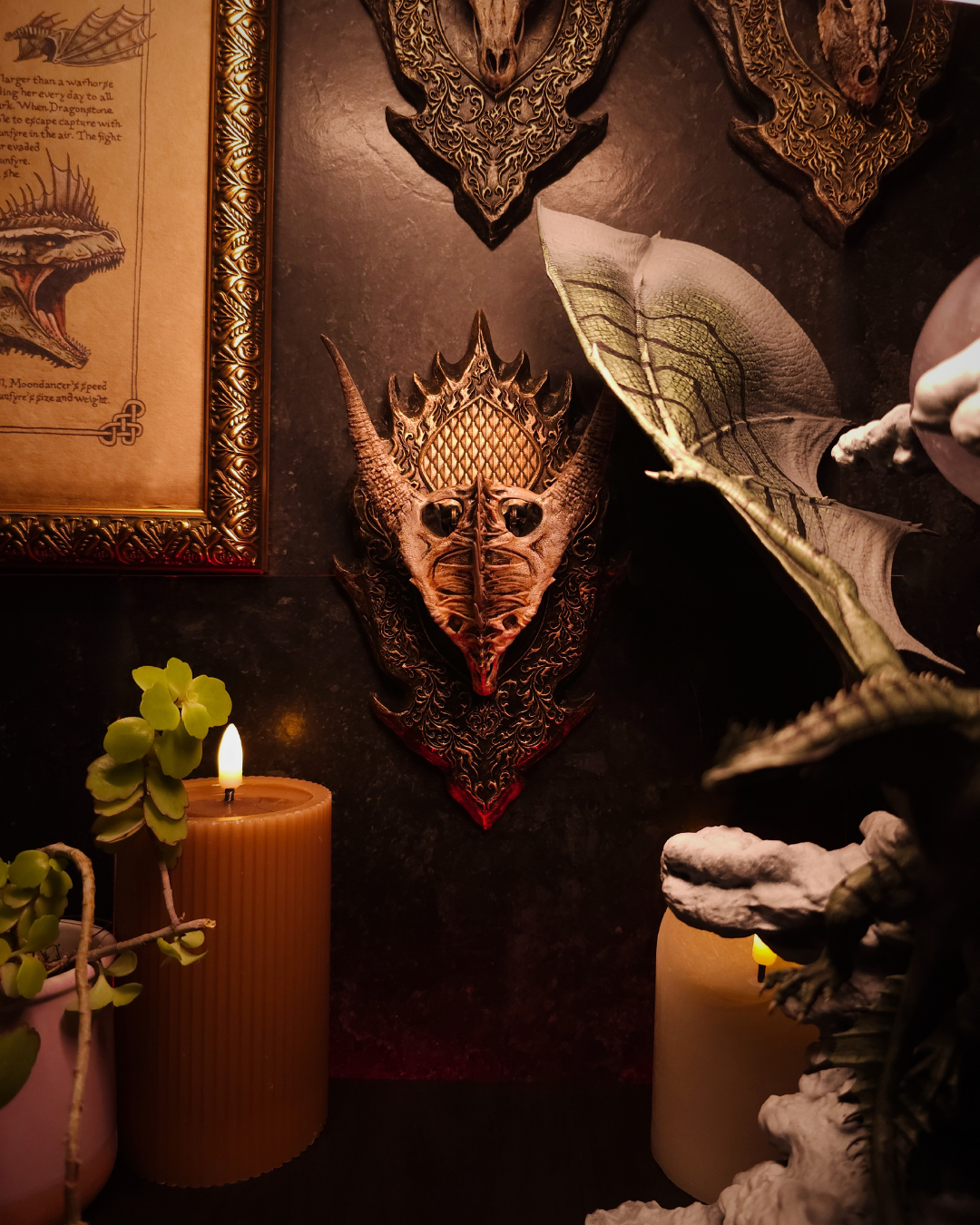 Trophée mural de crâne de dragon Moondancer présenté dans un décor fantasy complet, avec une figurine de dragon ailé au premier plan et des bougies allumées.
