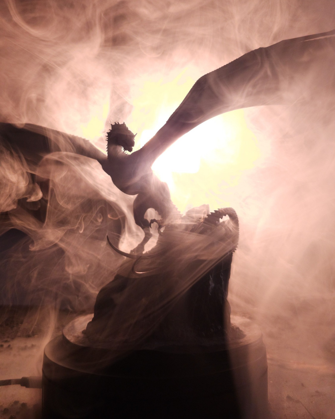 Figurine du dragon Greyghost éclairée par un effet lumineux et entourée de fumée dramatique.