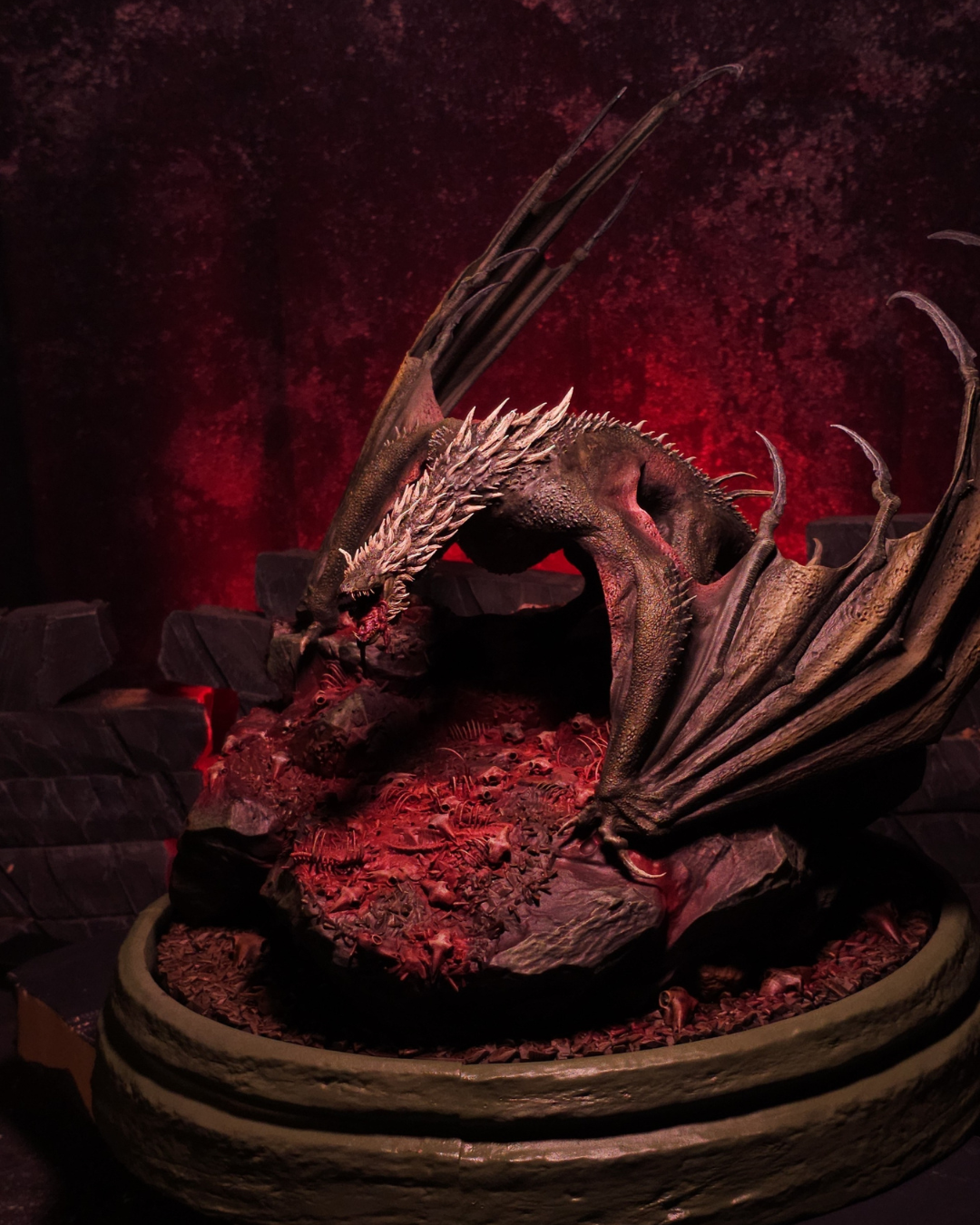 Vue en plongée du dragon Sheepstealer, sa tête tournée vers le sol jonché de squelettes, sublimée par un éclairage rouge sombre et un décor inspiré des enfers.