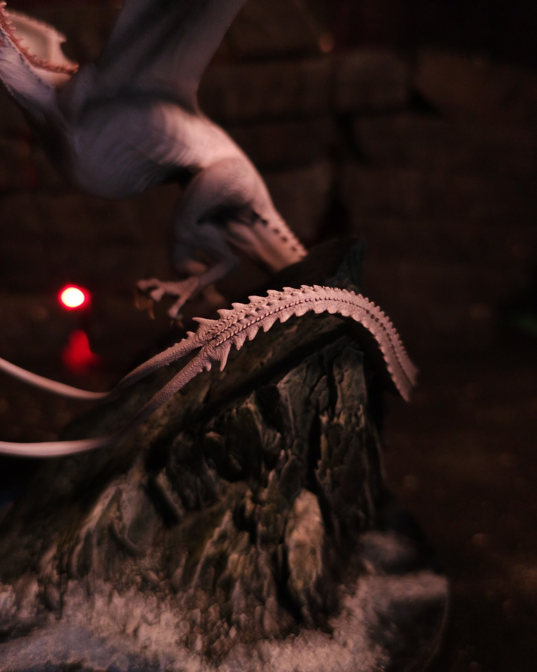Gros plan sur la queue hérissée du dragon Greyghost, posée sur le rocher de son socle.