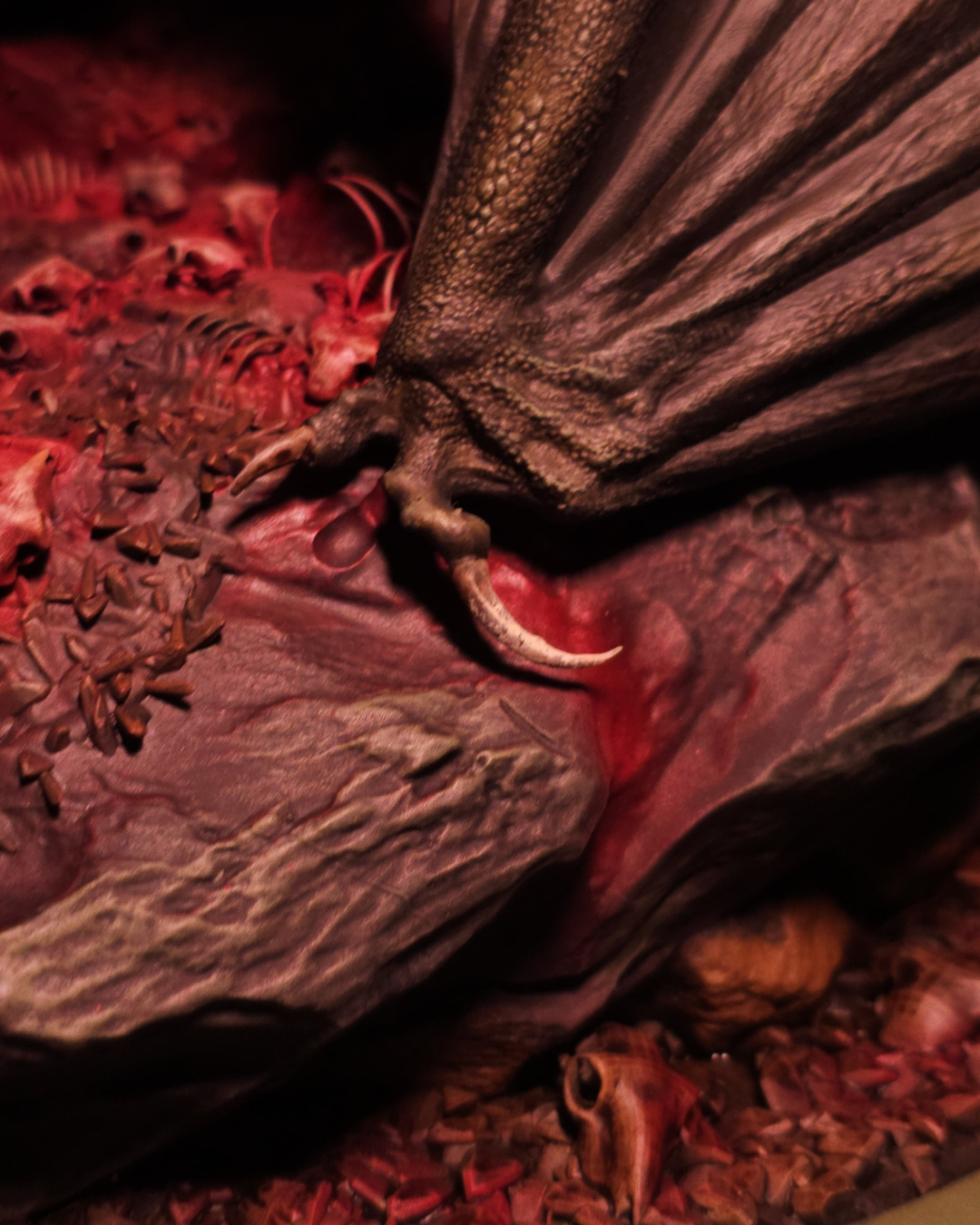 Gros plan sur la patte griffue du dragon Sheepstealer écrasant des crânes et des os, montrant la finesse du travail de sculpture et la teinte rouge sang du socle.