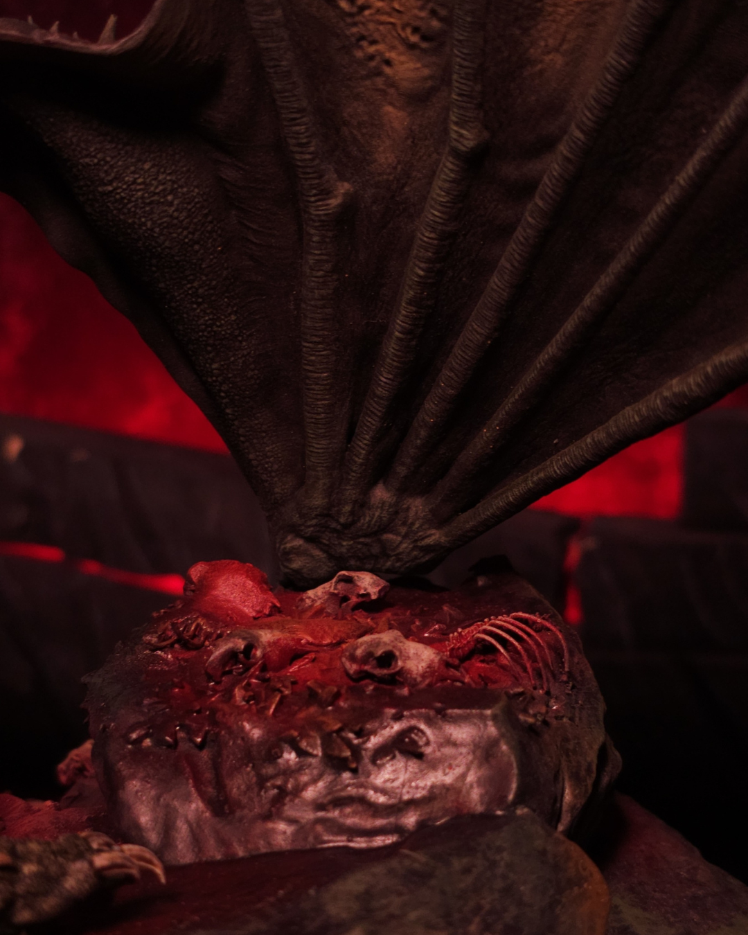 Vue rapprochée des ailes et griffes du dragon Sheepstealer posées sur un tas de crânes et d’ossements, dans une lumière rouge sombre d’Halloween.