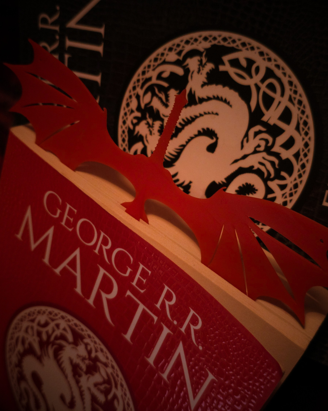 Marque-page en résine rouge en forme de dragon Caraxes posé sur le livre de George R.R. Martin.