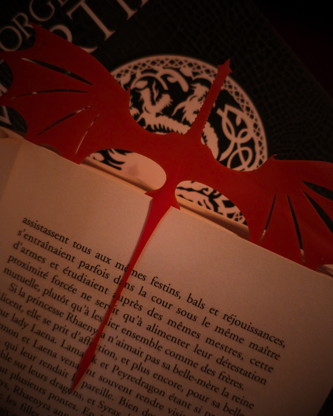 Marque-page dragon rouge Caraxes inséré entre les pages d’un roman de George R.R. Martin.