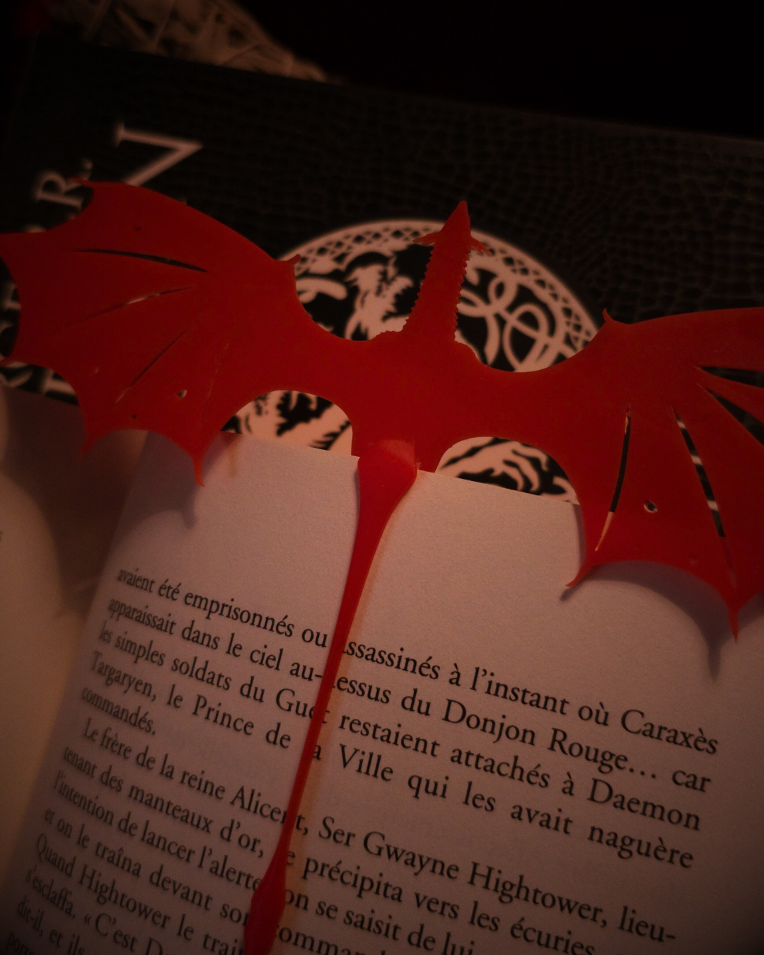Marque-page en forme de dragon rouge Meleys, dépassant élégamment entre les pages d’un livre Feu et Sang.