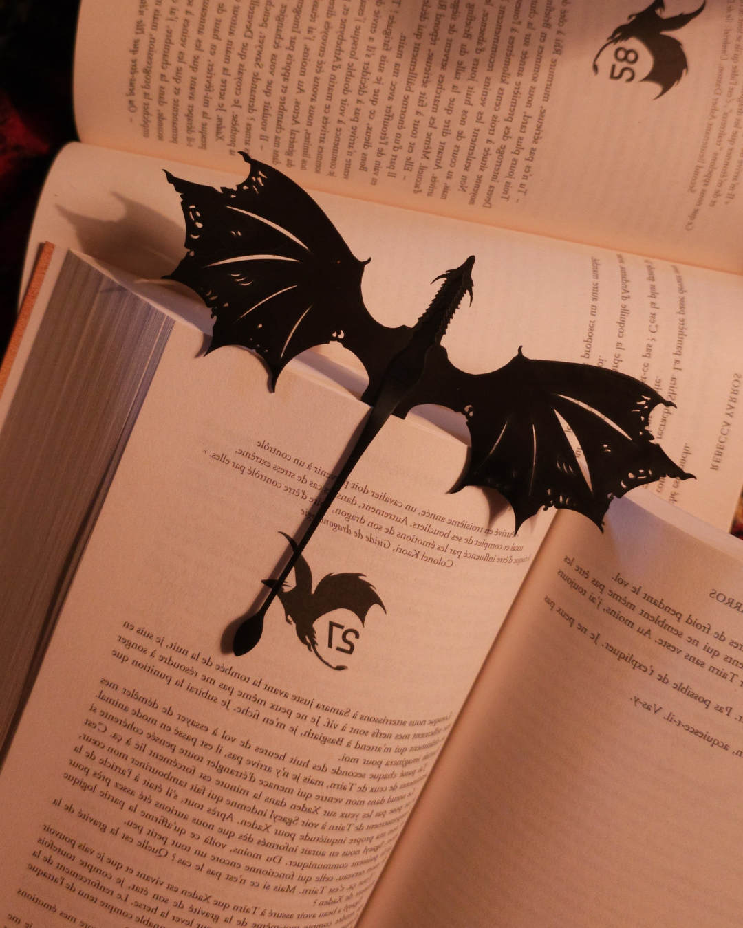 Marque-page dragon en résine noire glissé dans un roman, ambiance romantasy et fantasy, accessoire inspiré de Tairn de Fourth Wing.