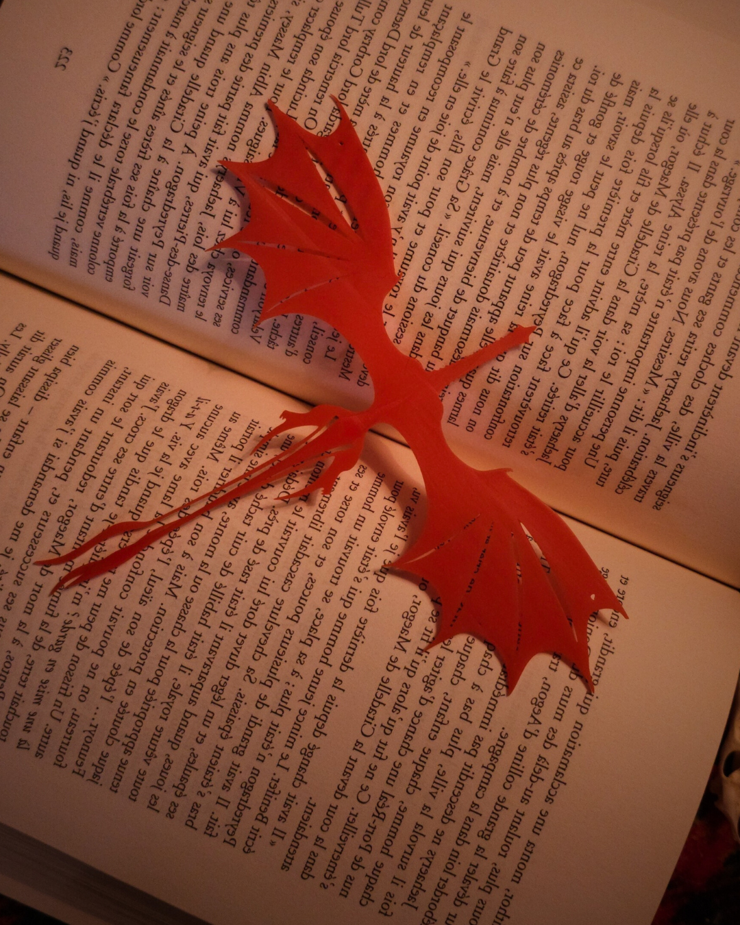 Marque-page rouge en forme de dragon Caraxes placé dans un livre ouvert, parfait pour les fans de fantasy.