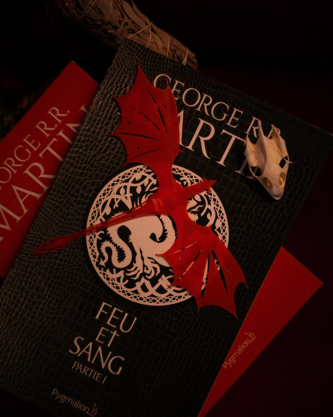 Marque-page en résine rouge inspiré du dragon Meleys, posé sur la couverture du roman Feu et Sang de George R.R. Martin.