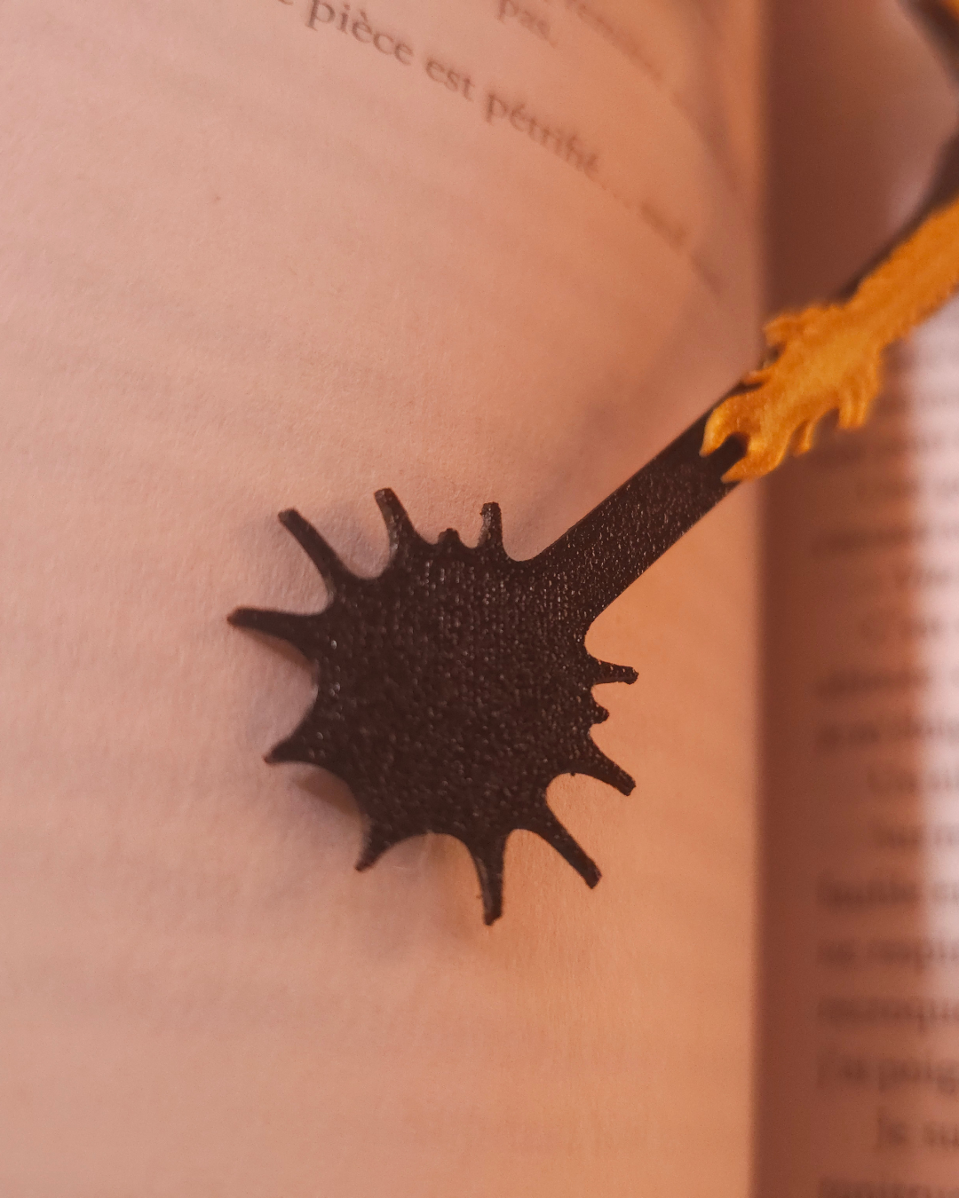 Gros plan sur la pince intégrée du marque-page dragon permettant de maintenir solidement les pages d'un roman de fantasy.