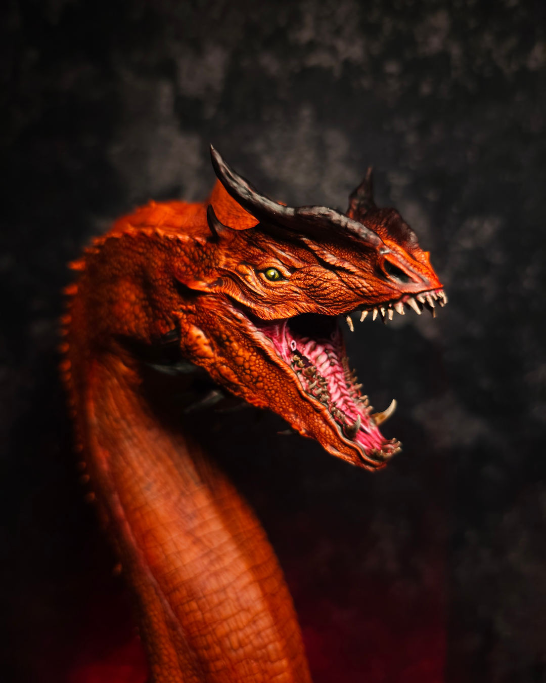 Portrait rapproché d’un dragon rouge aux yeux jaunes et à la gueule ouverte, mettant en avant la peinture artisanale et les détails réalistes de la sculpture.