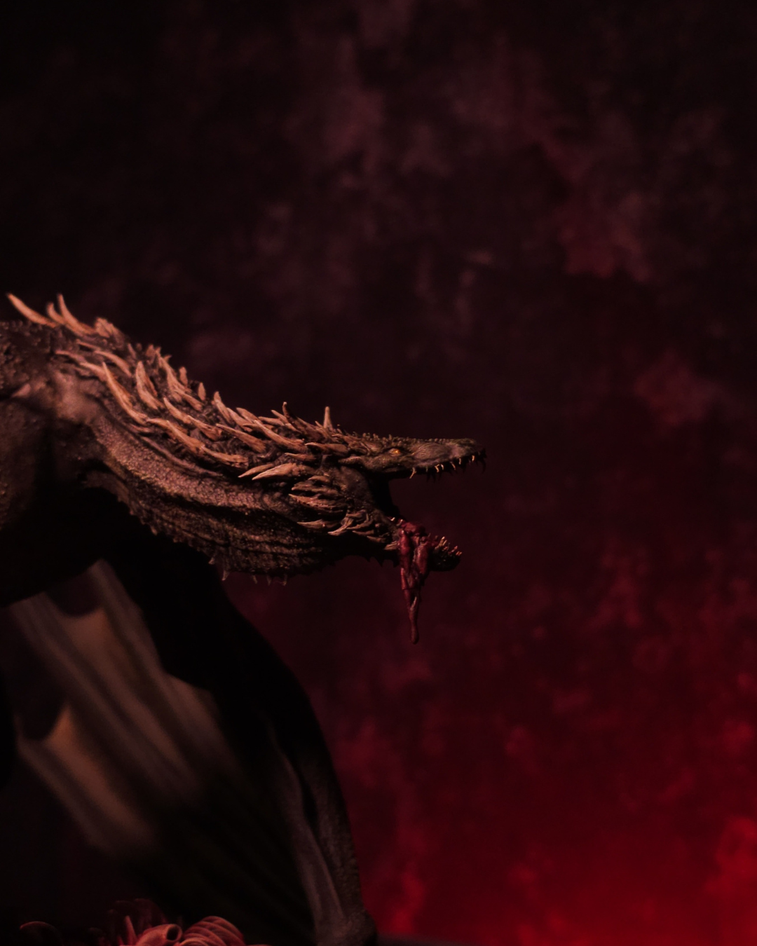 Tête du dragon Sheepstealer sortant de l’obscurité, gueule ouverte sur un morceau de chair, éclairée par une lumière rouge sombre d’Halloween.