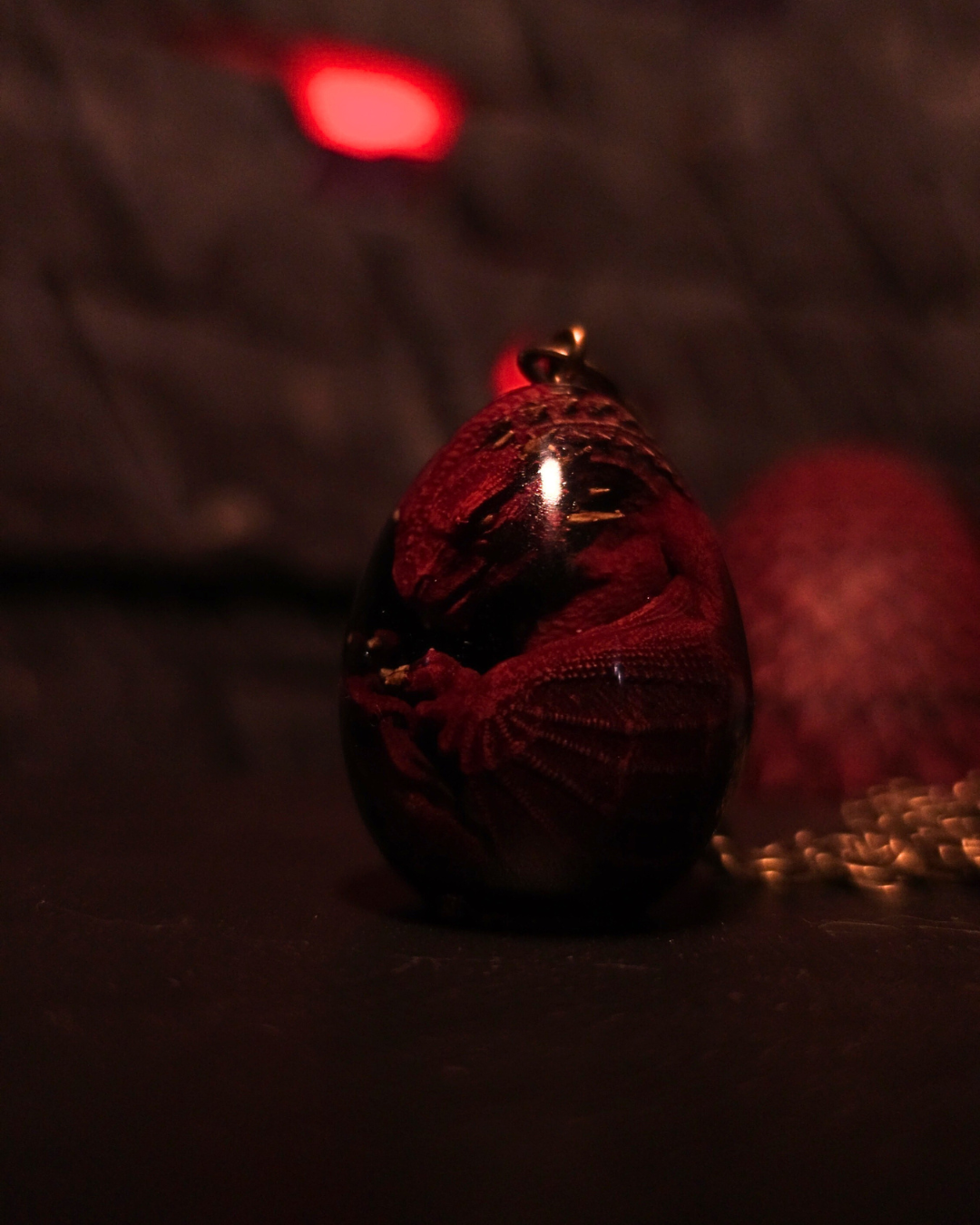 Pendentif fait main représentant un embryon de dragon rouge recroquevillé, coulé dans une résine en forme d'œuf