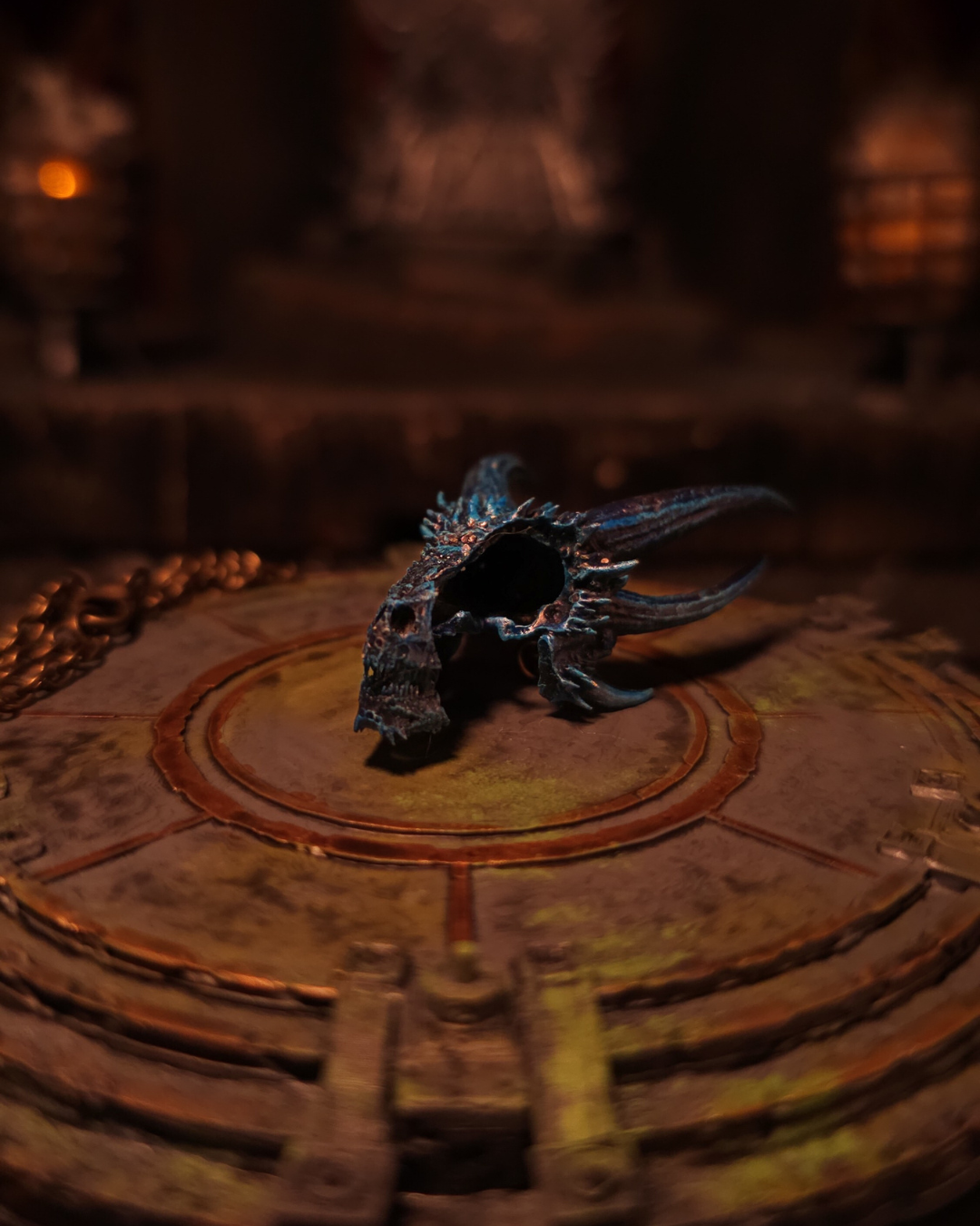 Vue oblique arrière du crâne de Viserion ; cornes incurvées et surface bleu nuit mouchetée d’argent, drapé sur sa chaîne dorée.