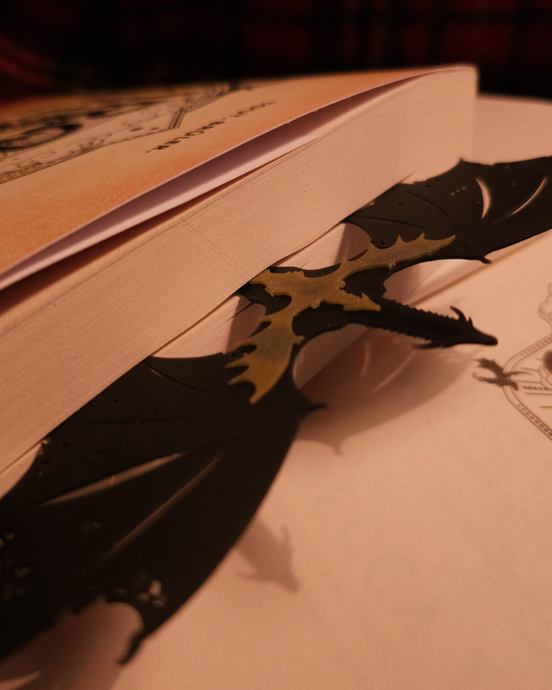 Vue rapprochée du marque-page dragon FourthWing, montrant la finesse des ailes et du corps en résine 3D. Le dragon est pris sous un livre, illustrant sa flexibilité et sa robustesse, idéale pour les lecteurs fantasy.