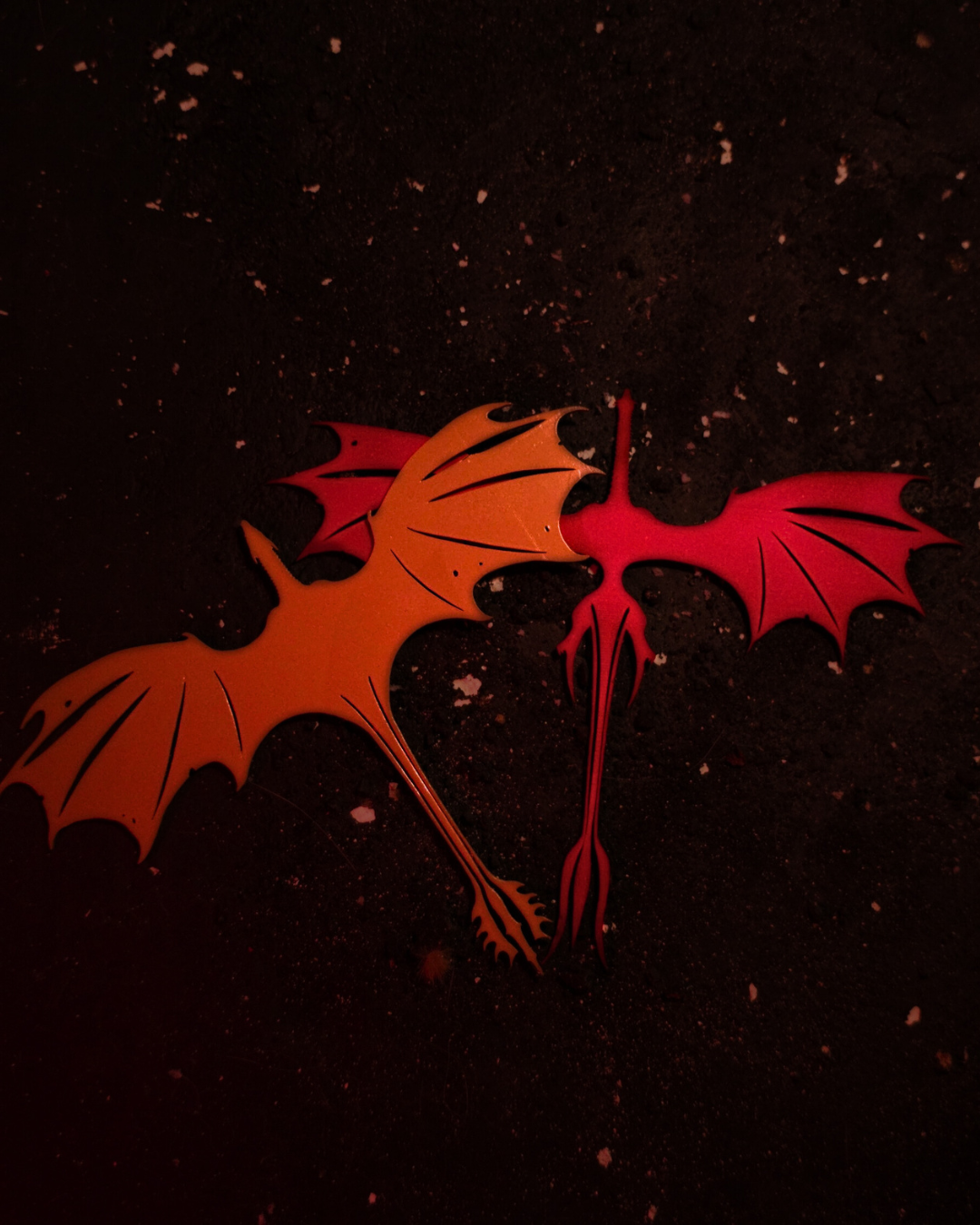 Bundle of two dragon bookmarks in red and orange laid flat on a dark speckled surface, showcasing their outstretched wings and tapered tails — perfect dragons bookmarks set.