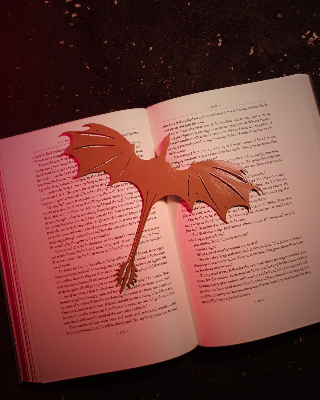 Orange Syrax-inspired dragon bookmark clipped into the center of an open fantasy novel, its sweeping wings and curled tail marking the page — ideal dragons bookmarks for immersive readers.