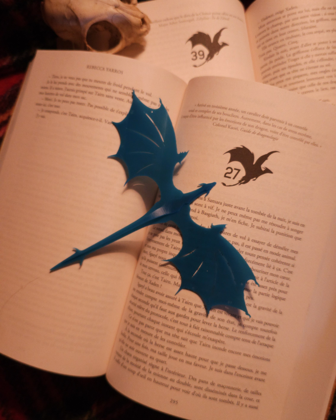Marque-page en forme de dragon bleu, inspiré de la saga Fourth Wing, posé sur un livre ouvert. Accessoire de lecture fantasy idéal pour les fans de romantasy et collectionneurs de figurines de dragon.