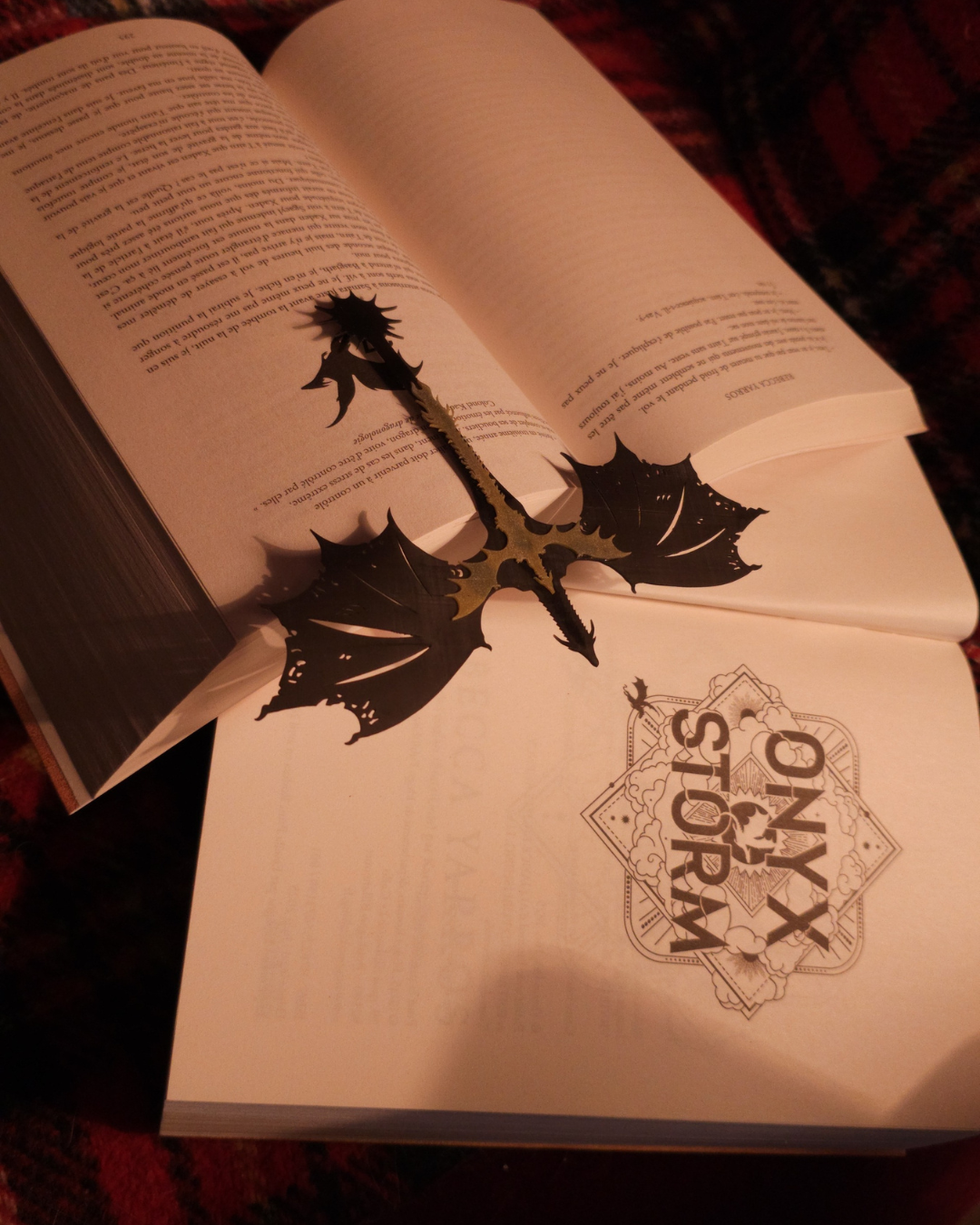 Le marque-page dragon Tairn + Andarna repose ouvert sur un livre, révélant sa silhouette détaillée et son mélange de noir et d’or. Un accessoire fantasy parfait pour accompagner une figurine de dragon dans une collection romantasy.