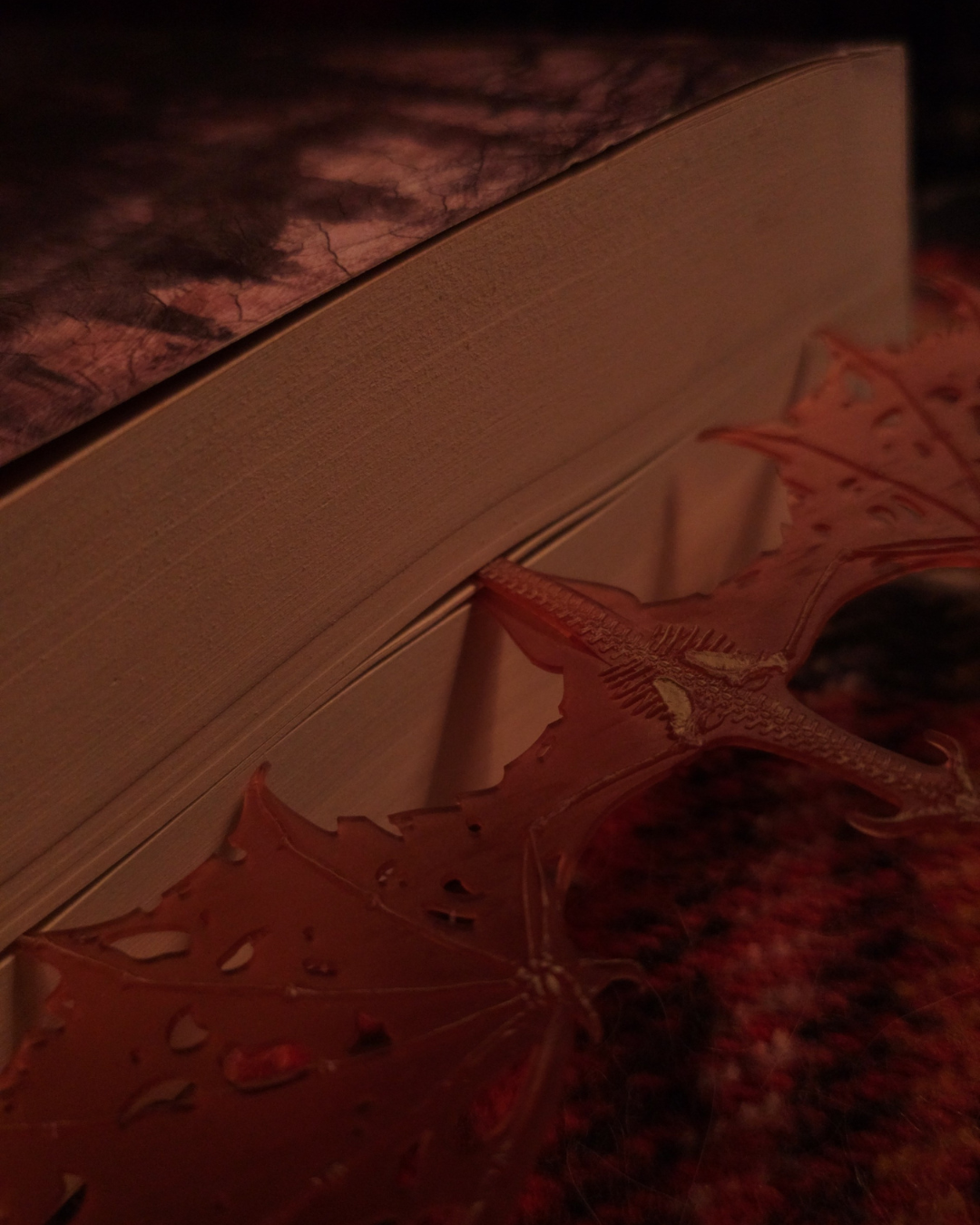 marques-pages dragon en résine rouge translucide glissé entre les pages d’un roman, dans une lumière chaude et tamisée évoquant l’ambiance d’halloween et la dark fantasy.